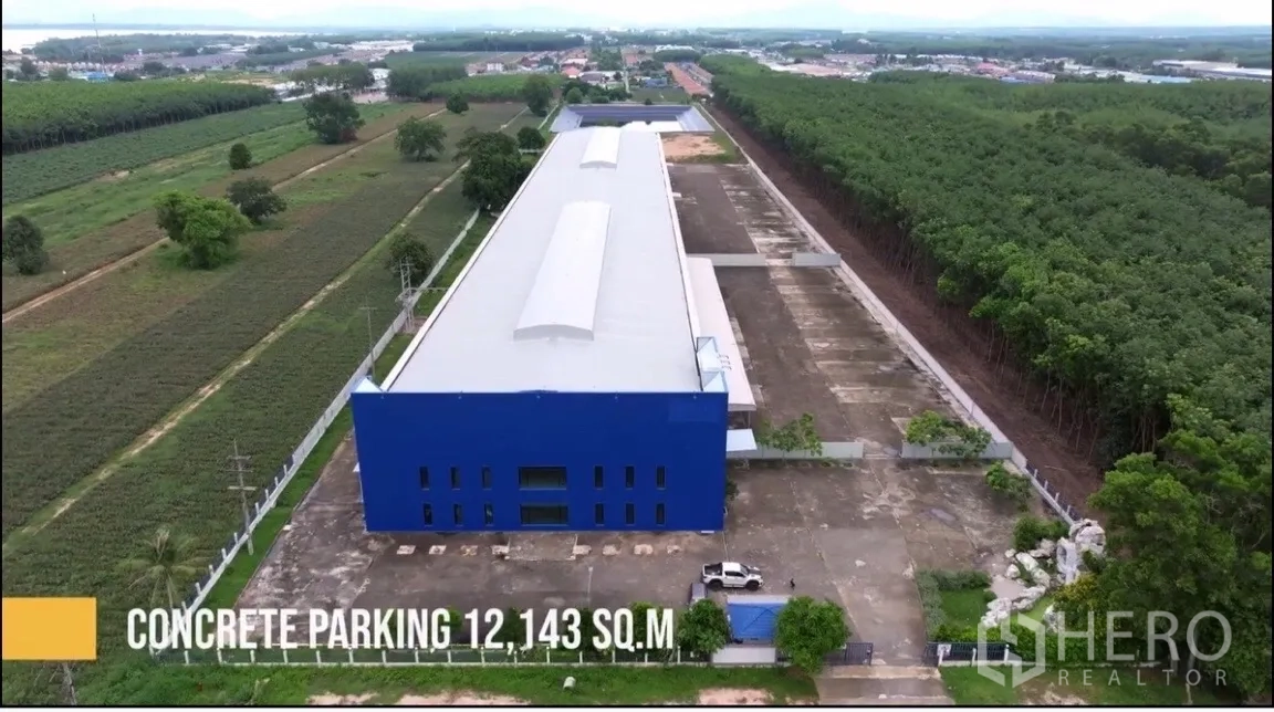 Factory for sale in Pluak Daeng, Rayong - Long rectangular factory complex with expansive concrete yard, perimeter wall, and tree-lined site seen from above.