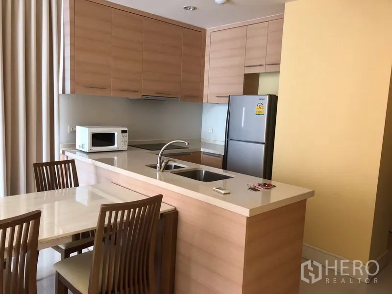 Condominium for rent or sale in Khlong Toei, Bangkok - Open-plan kitchen with light wood cabinets, breakfast bar with sink, and dining set.