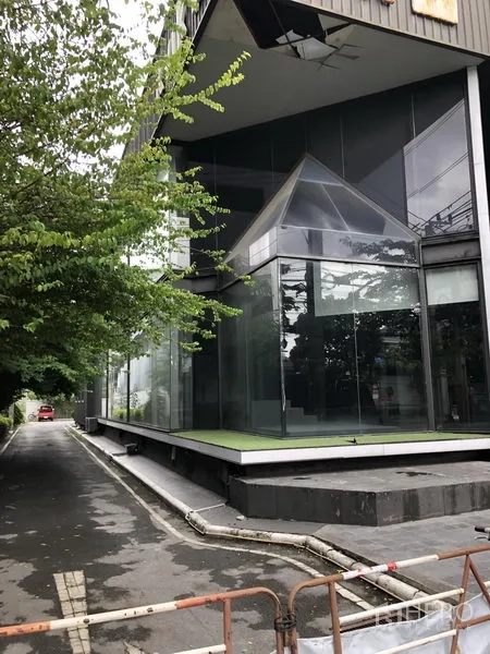 零售空间 出租在Watthana, Bangkok - 侧立面带雨棚的抬高平台与落地玻璃窗，旁有车道通行。