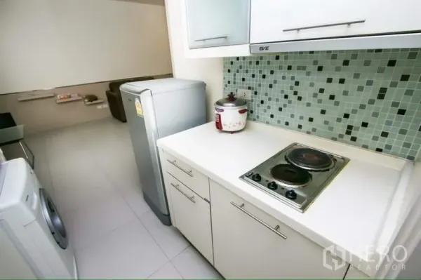 Condominium for rent in Ratchathewi, Bangkok - Kitchenette with electric cooktop, refrigerator, mosaic backsplash and washing machine overlooking the living area.