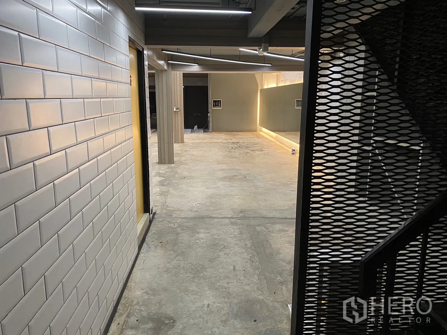 零售空间 出租在Phaya Thai, Bangkok - 走廊为白色地铁砖墙，金属网格楼梯，连接主开放区域。