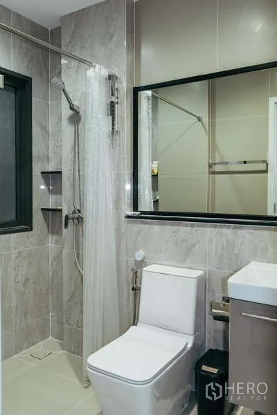 Detached House for sale in Sai Mai, Bangkok - Compact bathroom with shower enclosure, toilet and vanity in gray tiles.