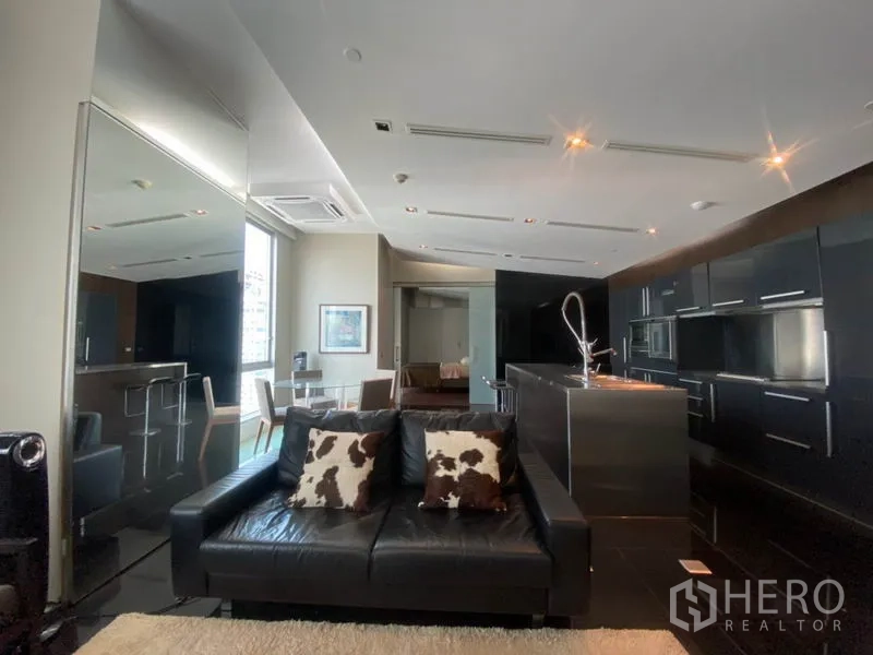 Condominium for rent in Sathon, Bangkok - Open living space with black leather sofa, stainless kitchen island and reflective finishes.