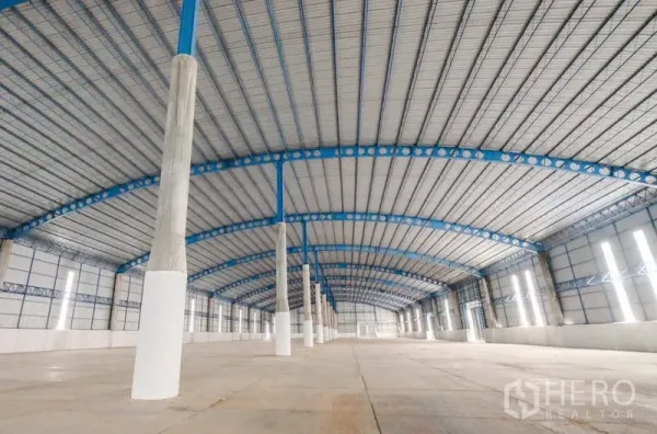 Warehouse for rent in Ban Pho, Chachoengsao - Long-span interior bay with blue roof beams, tall side windows, and open loading area.