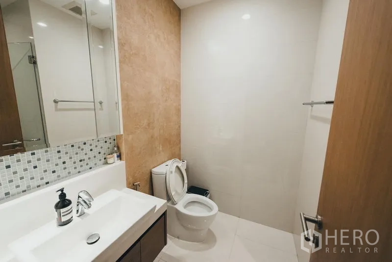 Condominium for rent in Khlong Toei, Bangkok - Guest bathroom featuring long vanity with mirror cabinets, mosaic splashback and toilet.