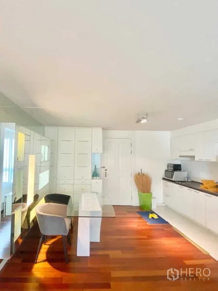 Condominium for rent in Watthana, Bangkok - Open living area with kitchenette, dining table, and full-height storage on warm wooden flooring.