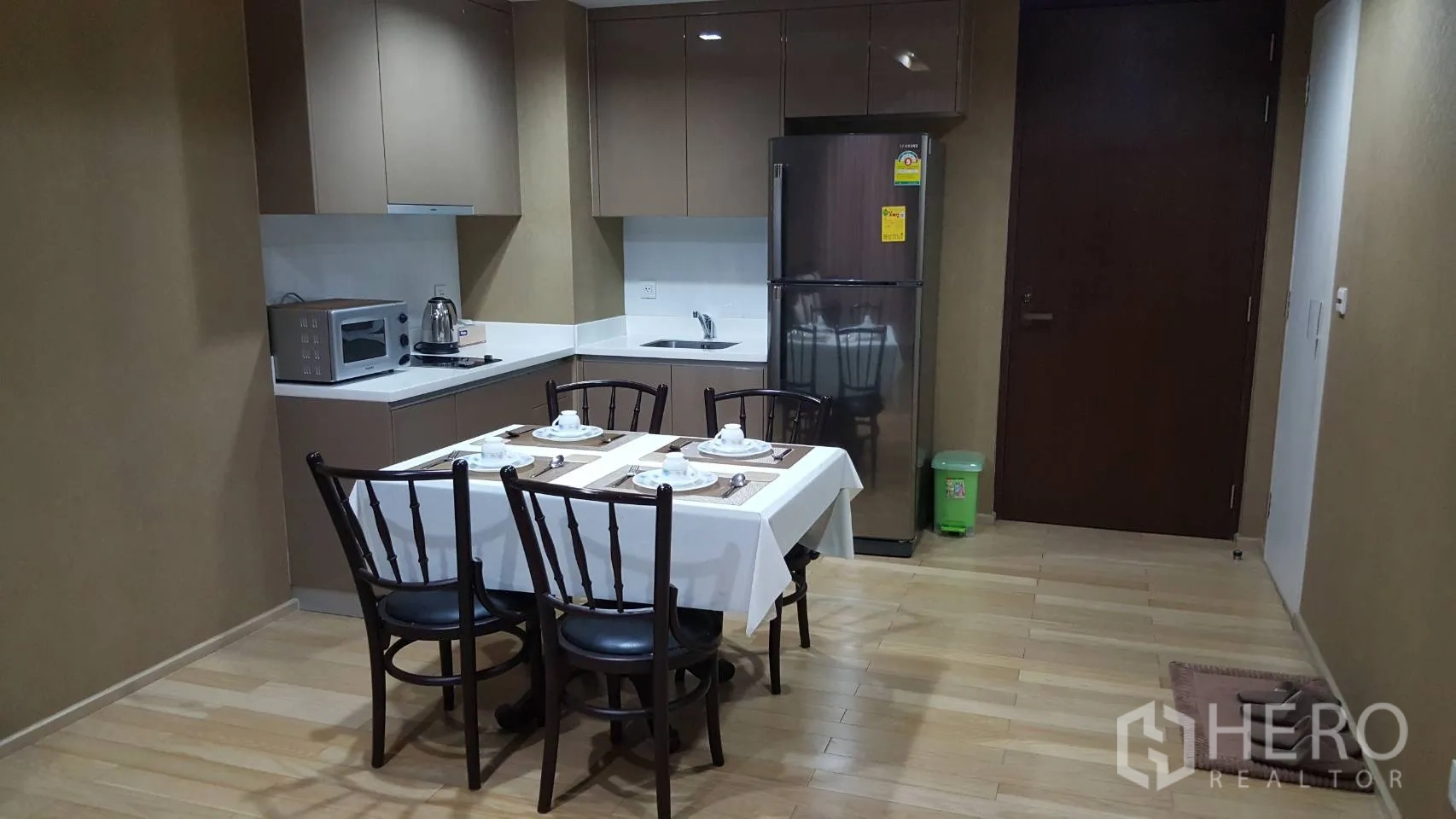 Condominium for rent in Khlong Toei, Bangkok - Compact L-shaped kitchen with fridge, microwave and four-seat dining table.
