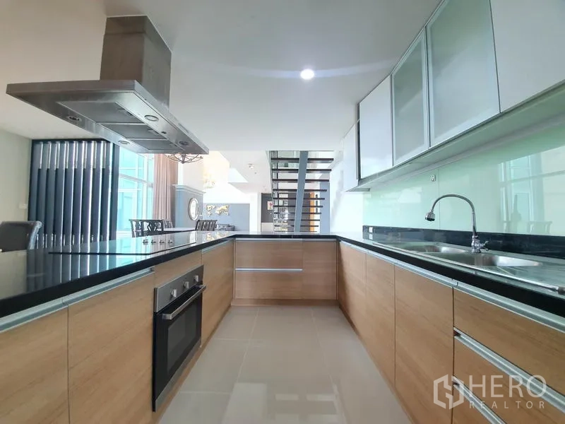 公寓 出租在Ratchathewi, Bangkok - U 型厨房，配烤箱、抽油烟机、黑色台面与木质橱柜。