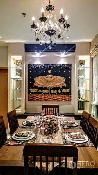 Condominium for rent in Khlong Toei, Bangkok - Formal dining table set under crystal chandelier with decorative wall art and lit display cabinets.
