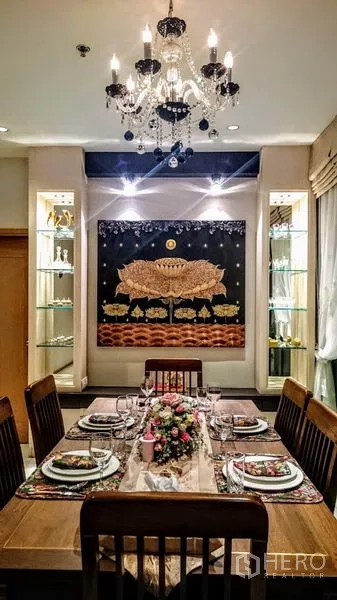 Condominium for rent in Khlong Toei, Bangkok - Formal dining table set under crystal chandelier with decorative wall art and lit display cabinets.