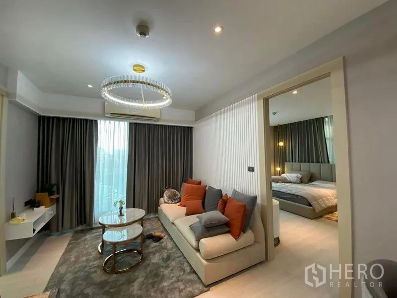 Condominium for sale in Huai Khwang, Bangkok - Living room with crystal-ring chandelier, sliding door to bedroom and floor-to-ceiling curtained window.