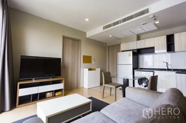 公寓 出租在Watthana, Bangkok - 开放式客厅，灰色沙发、电视柜与带冰箱和洗衣机的一体化厨房