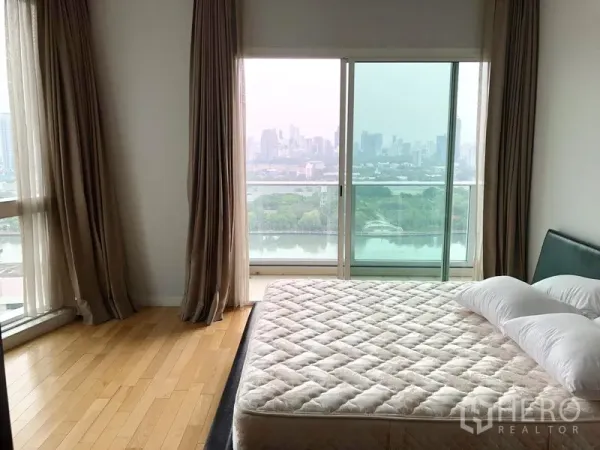 Condominium for rent in Khlong Toei, Bangkok - Bedroom with balcony and floor-to-ceiling windows overlooking lake and city skyline.