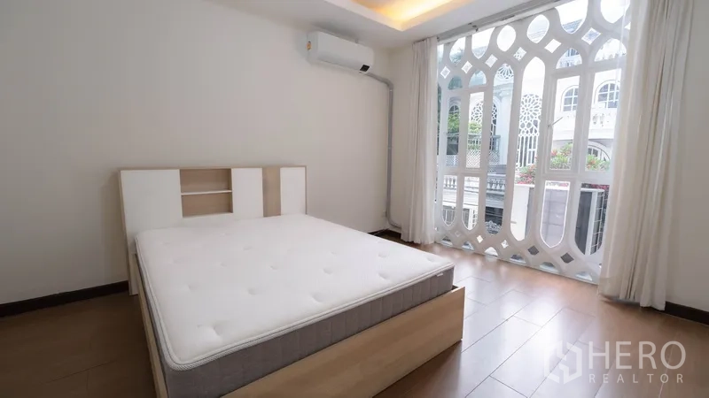 Townhouse for rent in Watthana, Bangkok - Bedroom with a large window and patterned screen opening to a balcony.