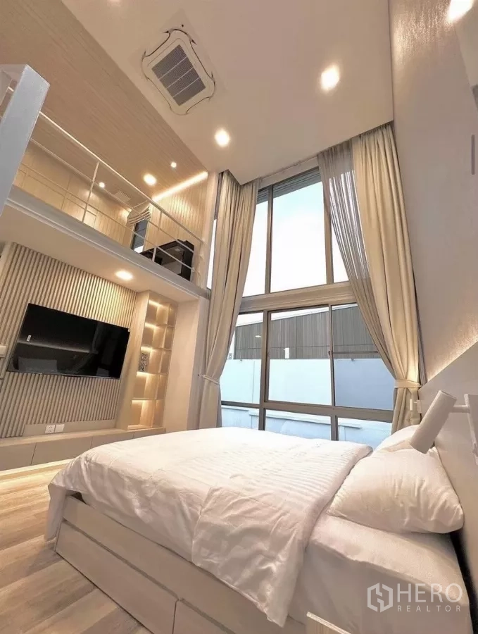 Detached House for rent in Saphan Sung, Bangkok - Bright bedroom with tall windows, TV wall and staircase to a lofted area.