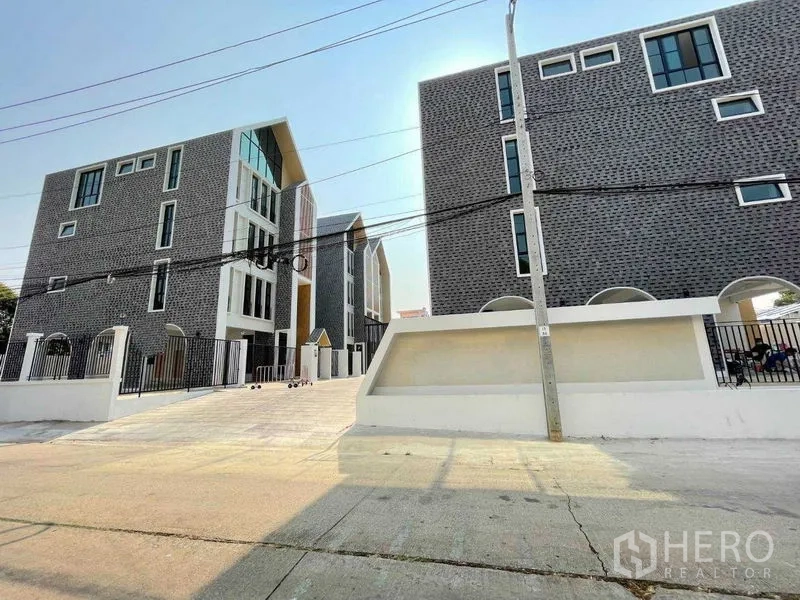 带办公室的家 出租在Bang Kapi, Bangkok - 现代化围合式住宅办公楼群，砖纹立面与宽阔车道。