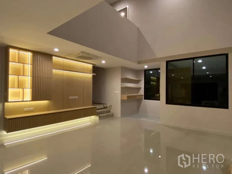 Townhouse for rent or sale in Saphan Sung, Bangkok - Double-height living room with cove lighting, floating shelves and large windows.