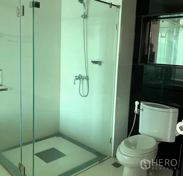 Condominium for rent in Pathum Wan, Bangkok - Modern bathroom featuring a glass-enclosed shower, white toilet, and sleek monochrome tiles.