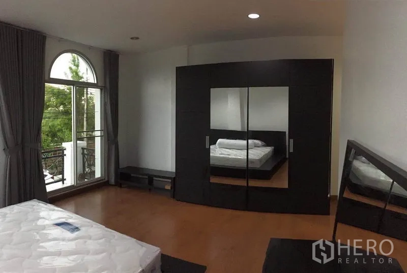 Townhouse for rent in Lat Phrao, Bangkok - Master bedroom with large wardrobe, mirror and wood flooring.