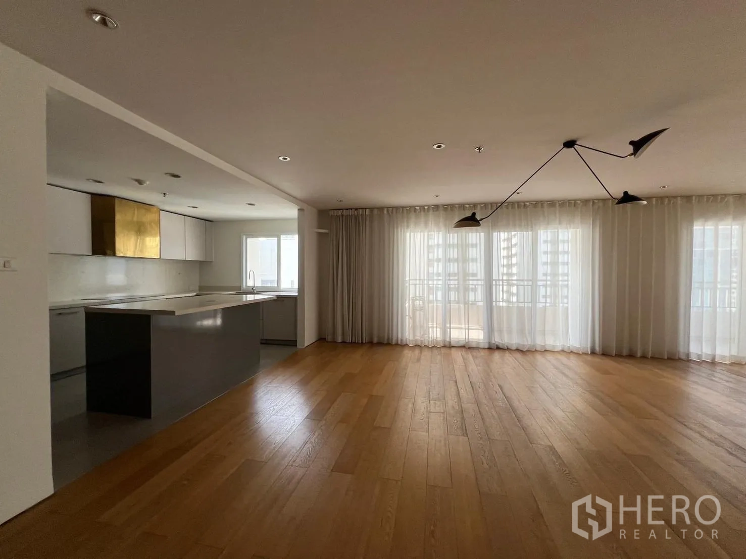 Condominium for rent or sale in Sathon, Bangkok - Open living area adjoining an island kitchen with sheer curtains and balcony doors.