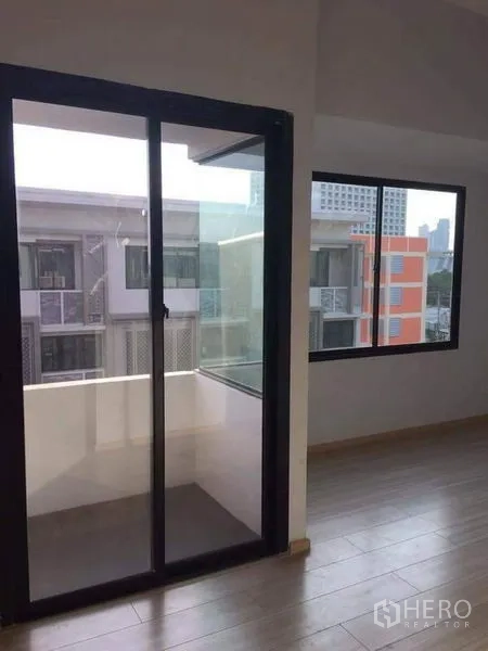 Townhouse for sale in Yan Nawa, Bangkok - Room with sliding glass door to a small balcony and corner window, wood flooring throughout.