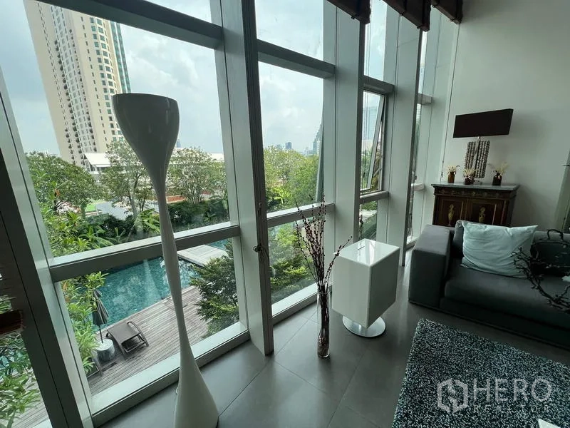 Condominium for sale in Khlong San, Bangkok - Floor-to-ceiling windows overlooking the pool deck, trees, and city skyline.