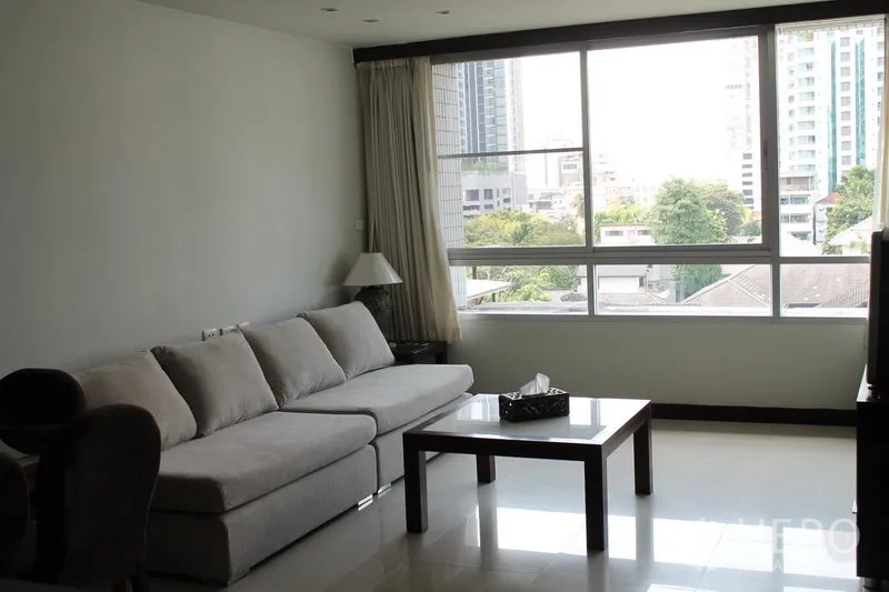 Apartment for rent in Bang Rak, Bangkok - Living room with wide window, long sofa and coffee table facing city views.