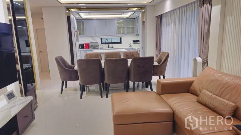Detached House for sale in Sai Mai, Bangkok - Open-plan living and dining area with leather sofa and eight-seat table beside full-height curtains.