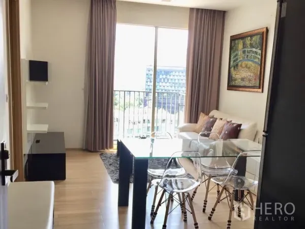 Condominium for rent in Khlong Toei, Bangkok - Bright living and dining area with glass table, wood floors, and balcony city view.