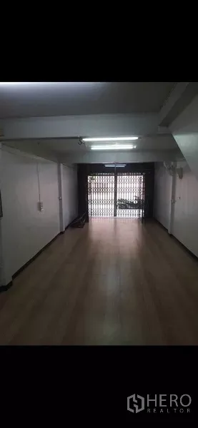 Shophouse for rent or sale in Phra Khanong, Bangkok - Long shop interior facing the metal folding gate with bright fluorescent lighting.