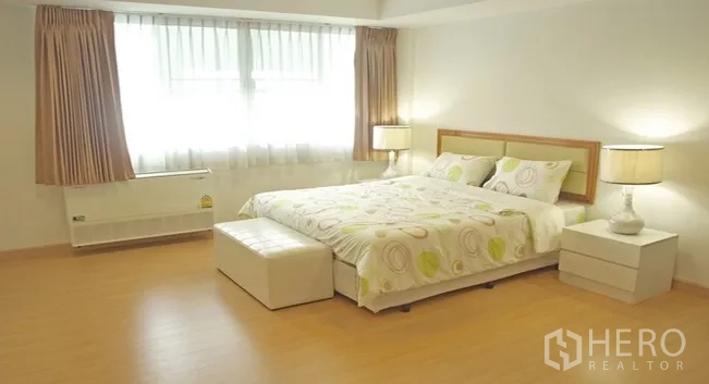 Apartment for rent in Khlong Toei, Bangkok - Spacious master bedroom with large windows, soft curtains and ottoman at the foot of the bed