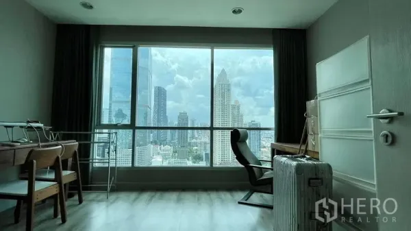 Condominium for sale in Sathon, Bangkok - Bright room used as bedroom or home office with desk and chair facing a panoramic Bangkok skyline through a wide window.