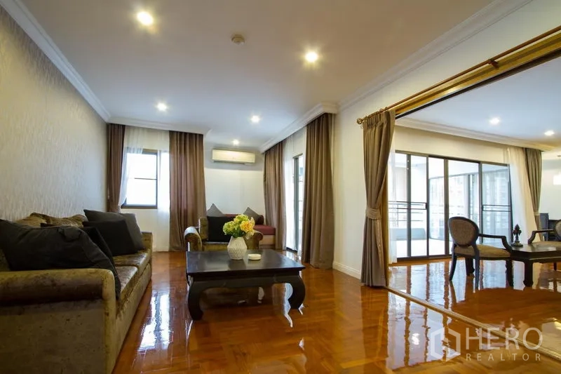 Apartment for rent in Watthana, Bangkok - Cozy lounge with sofas, coffee table, balcony access, and wide windows with curtains.