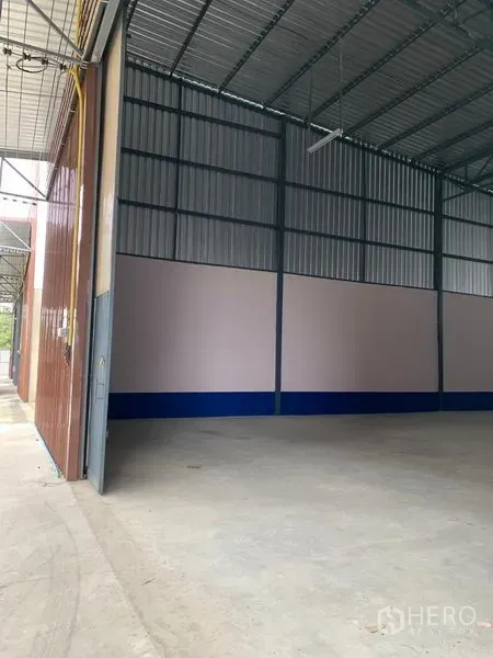 Warehouse for rent in Saphan Sung, Bangkok - Large sliding metal door opening to a warehouse with covered loading area and a tall metal roof structure.