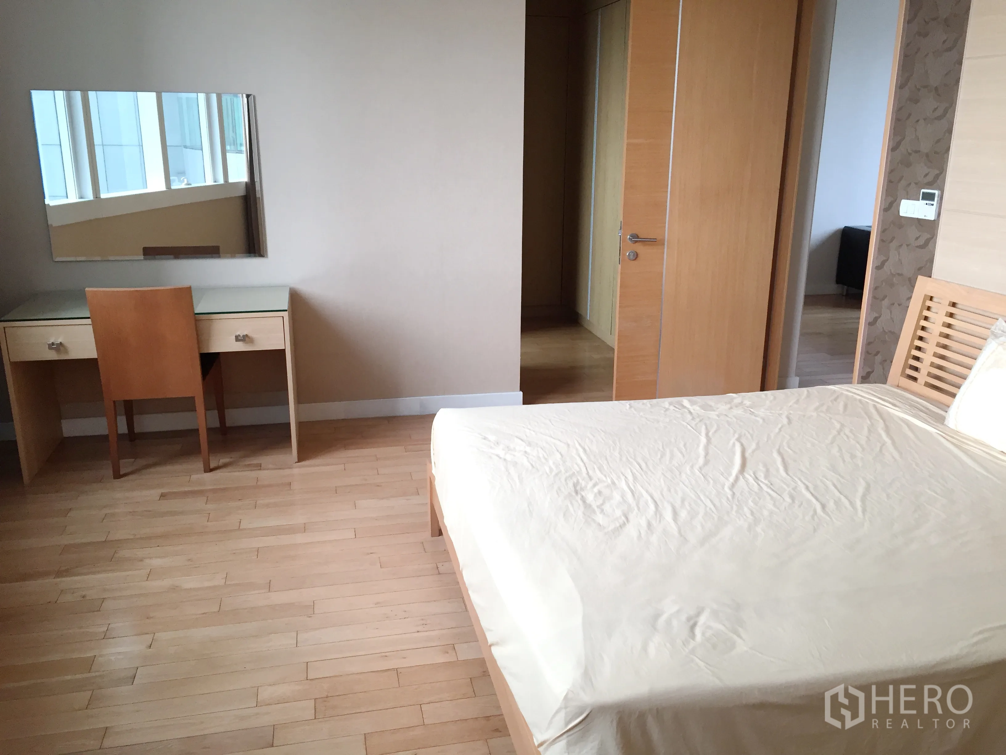 Condominium for rent in Khlong Toei, Bangkok - Primary bedroom with wood bed, dressing desk and built-in wardrobe.