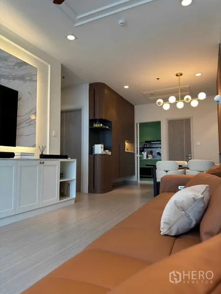 Condominium for rent in Bang Rak, Bangkok - Living area looking toward dining and kitchen with brown leather sofa, modern chandelier and recessed lighting.