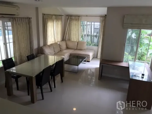 独立式住宅 出租在Khlong Sam Wa, Bangkok - 采光良好的起居区，转角沙发、餐桌，窗外是绿意花园。