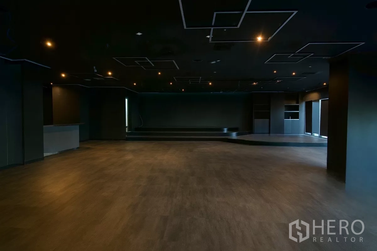Retail Space for rent - Large retail hall featuring a dark ceiling with recessed lighting and a raised stage at the far end.