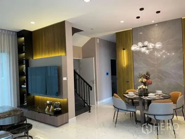 独立式住宅 出租在Bang Phli, Samut Prakan - 客餐厅一体，电视背景墙、大理石地面与现代吊灯，旁为楼梯。