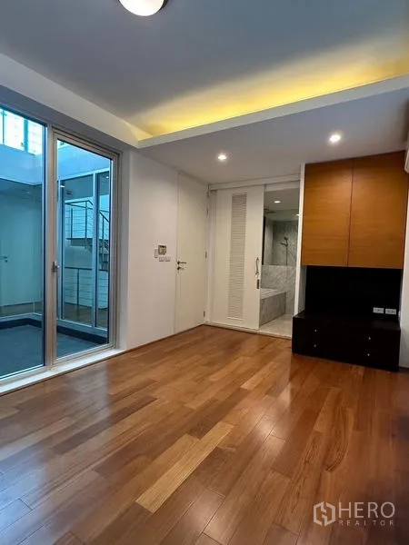 Townhouse for sale in Yan Nawa, Bangkok - Bedroom with warm wooden flooring, built-in cabinetry, recessed lighting and sliding door to the bathroom.
