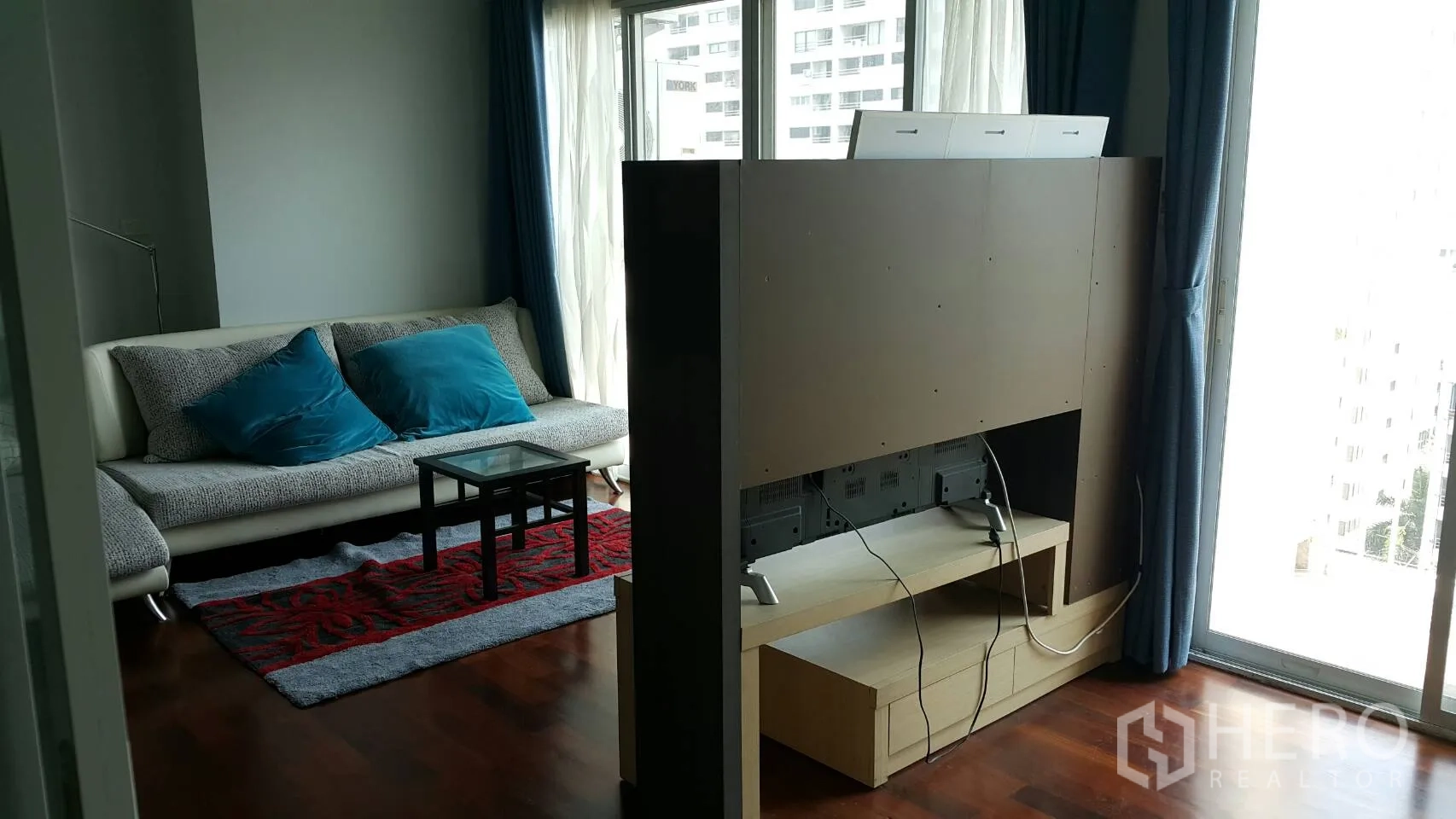 公寓 出租在Watthana, Bangkok - 客厅电视隔断与落地窗，蓝色窗帘，可见城市景观。