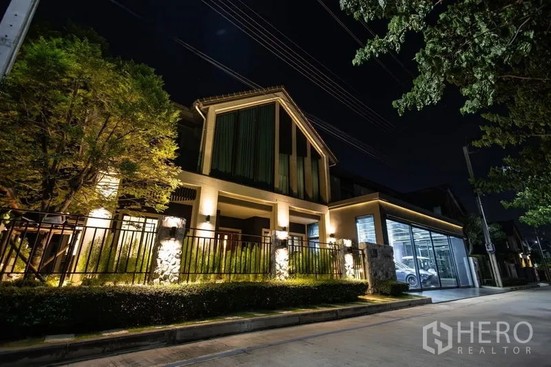 独立式住宅 出售在Pak Kret, Nonthaburi - 夜景外立面，暖色建筑照明与玻璃车库。