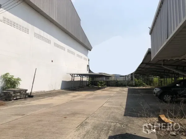 工厂 出租在Mueang Samut Prakan, Samut Prakan - 工厂建筑之间的宽阔混凝土场地，带有遮棚停车位与卡车通道。