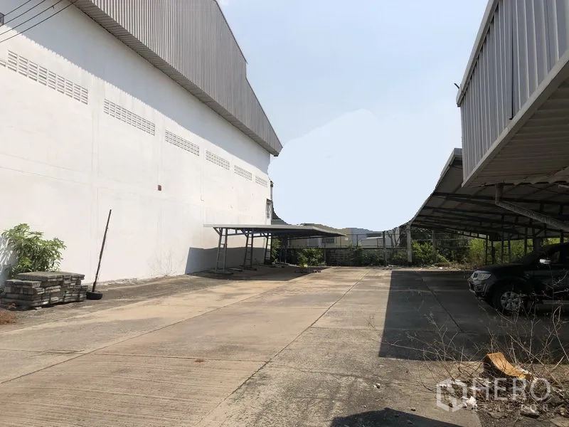工厂 出租在Mueang Samut Prakan, Samut Prakan - 工厂建筑之间的宽阔混凝土场地，带有遮棚停车位与卡车通道。