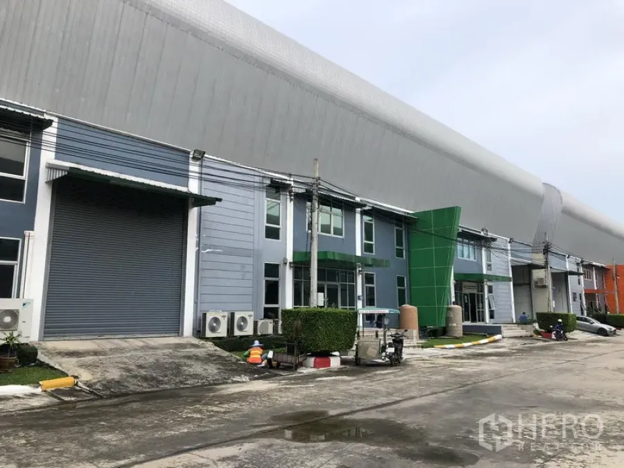 Factory for rent in Samut Prakan - Row of modern factory units with roller shutters, office fronts and an 8‑meter access road.