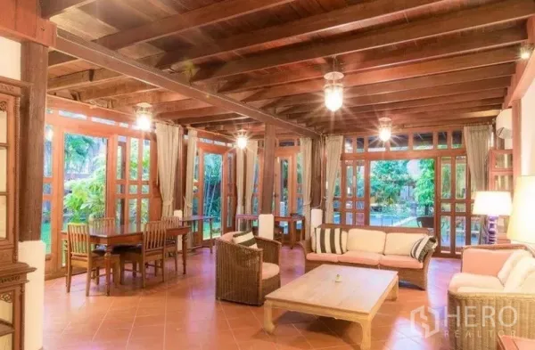 Detached House for rent in Bang Na, Bangkok - Spacious Thai‑style living and dining room with timber beams, terracotta floors, large windows and garden views in Bang Na house.