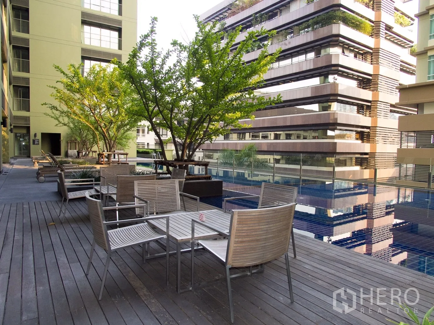 Condominium for rent or sale in Watthana, Bangkok - Condominium pool deck with seating areas, trees and a reflective swimming pool.