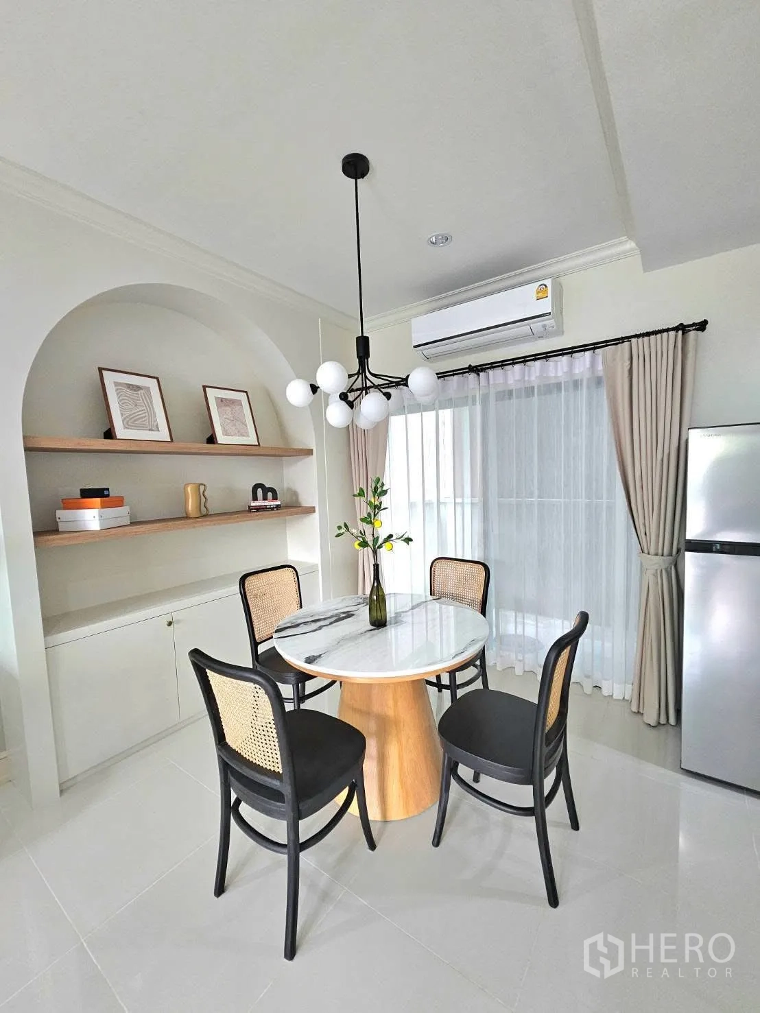 Townhouse for rent in Saphan Sung, Bangkok - Cozy dining corner with a marble round table, four rattan-back chairs, modern pendant light, shelves, and sheer curtains.