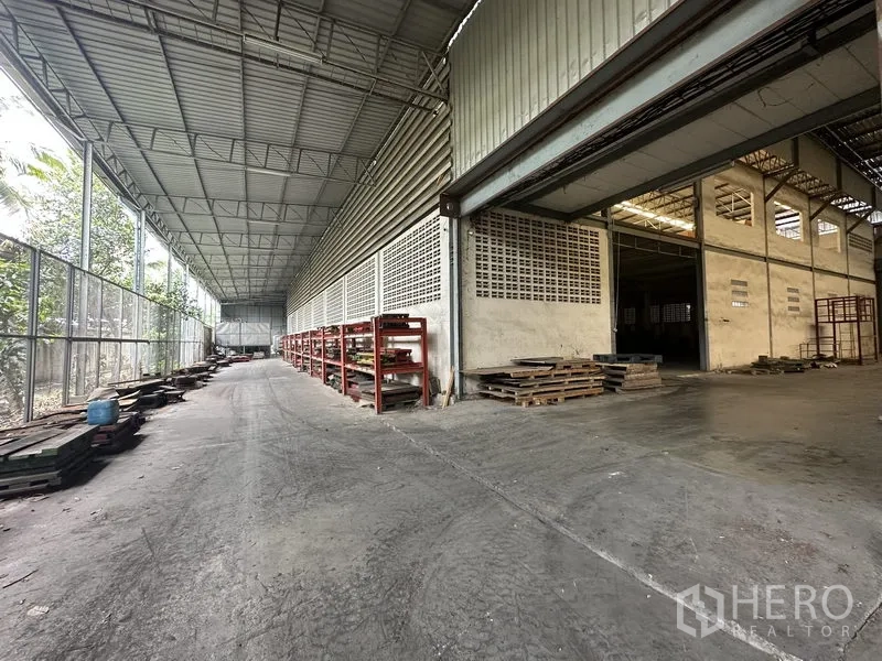 Factory for rent or sale in Lam Luk Ka, Pathum Thani - Covered side loading bay with mesh walls and red storage racks.