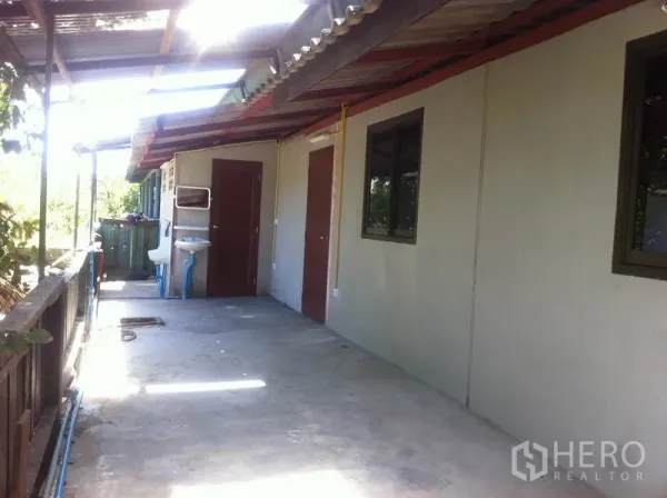 Warehouse for rent in Lam Luk Ka, Pathum Thani - Covered side corridor with doors, windows, outdoor sink, and railing beside green surroundings.